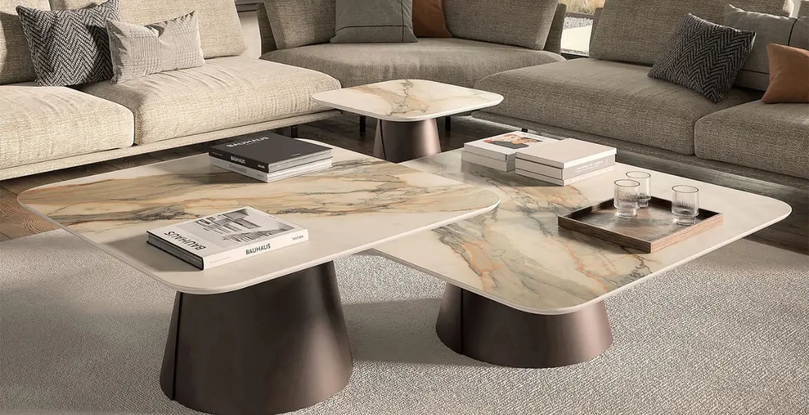 Elegant set of square marble coffee tables with natural veining, supported by modern bronze-finished cone-shaped bases, perfectly complementing a contemporary living room with neutral-toned seating.