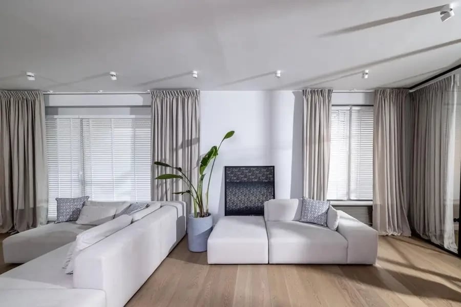 Modern living room featuring heavy linen curtains in soft neutral tones, paired with white minimalist furniture and a large potted plant, creating a serene and contemporary atmosphere.