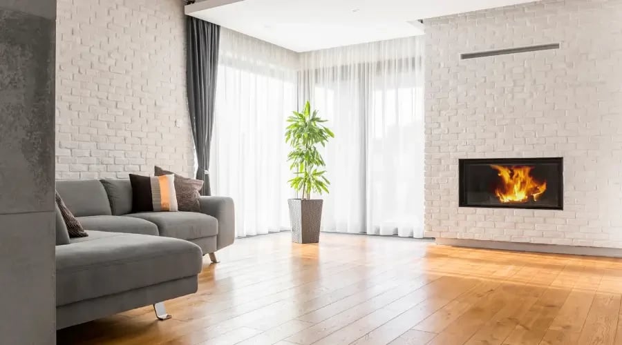 Modern living room with floor-to-ceiling sheer curtains, allowing natural light to flood the space, complemented by minimalist furniture, a plant, and a sleek fireplace for a cozy, contemporary atmosphere.