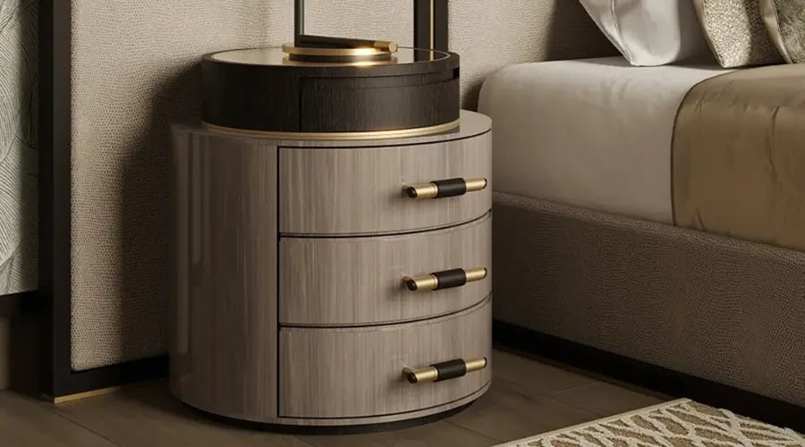 Luxury round nightstand with three drawers, elegant wood finish, and gold accents, placed beside a modern upholstered bed.