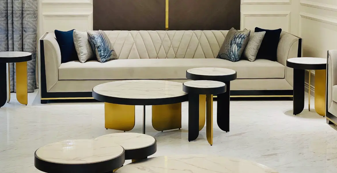 Luxury beige sofa with gold and black accents, paired with round marble-top coffee tables featuring gold and black metal bases, creating an elegant and sophisticated living room setting.