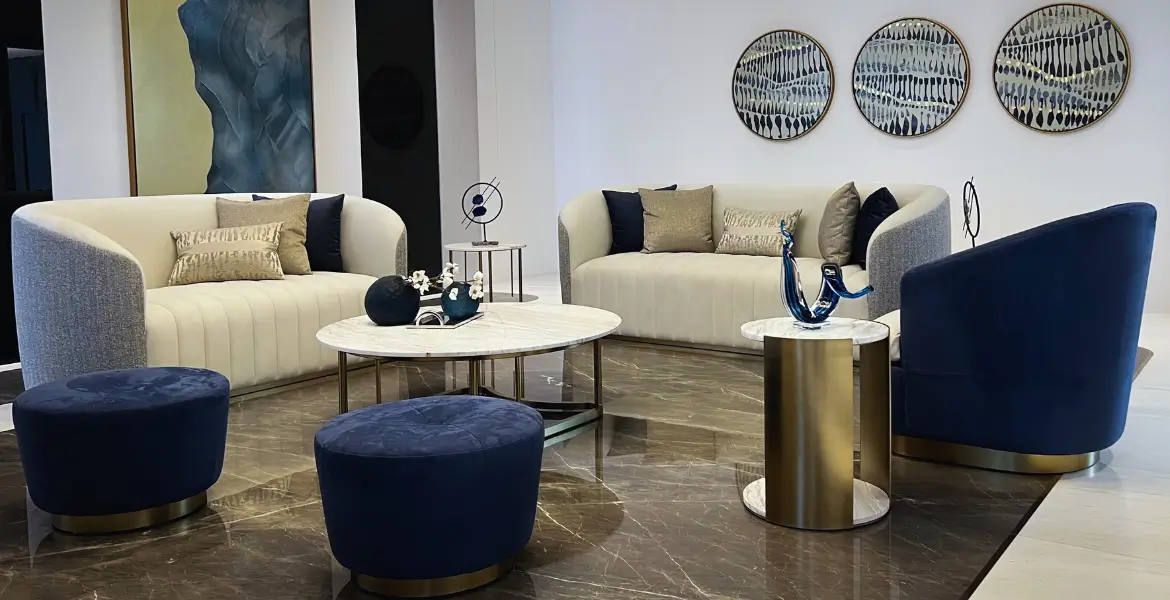 Elegant luxury living room featuring curved beige sofas, blue velvet seating, and gold-accented marble tables, creating a stylish and comfortable space that enhances aesthetics, comfort, and durability.