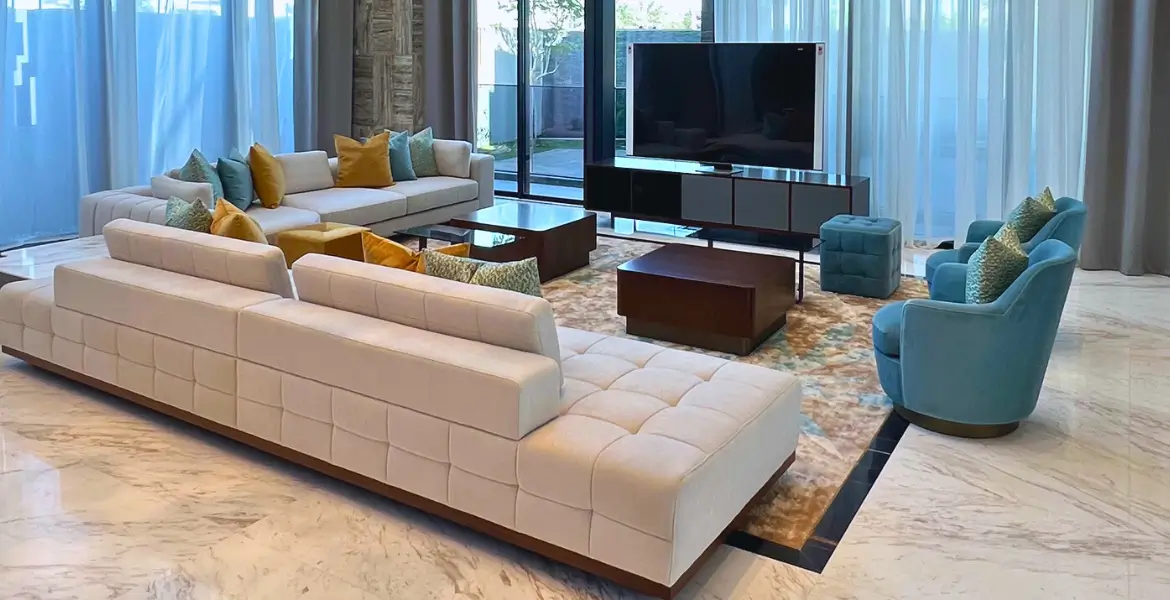 Luxury modern villa living room in UAE featuring custom modern furniture, large white sectional sofas, accent chairs in teal, and wooden coffee tables, designed by BOLD Bespoke Design.
