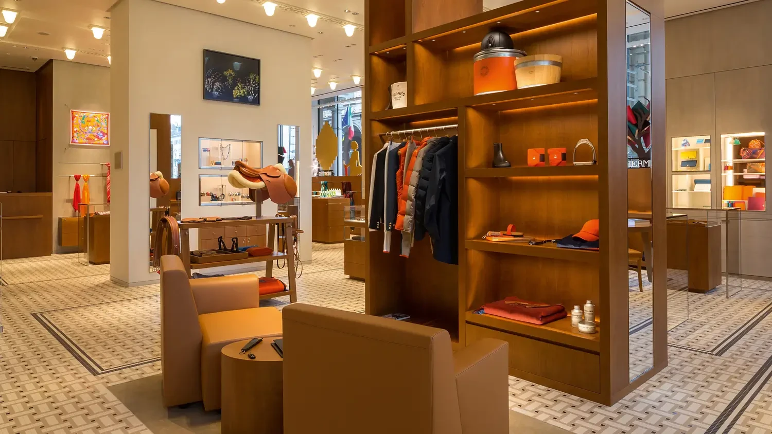 Luxury boutique interior with warm wood shelving, designer clothing, accessories, and leather goods on display. The space features elegant seating, accent lighting, and a sophisticated, modern atmosphere.