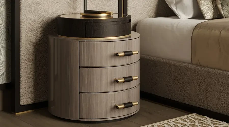 Luxury round nightstand with three drawers, elegant wood finish, and gold accents, placed beside a modern upholstered bed.