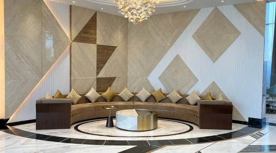 صوفا دائرية فاخرة في مدخل عصري، مع طاولة وسط رخامية ولمسات ديكور هندسية على الجدران، وألوان محايدة أنيقة تعكس الفخامة في تصميم داخلي راقٍ.