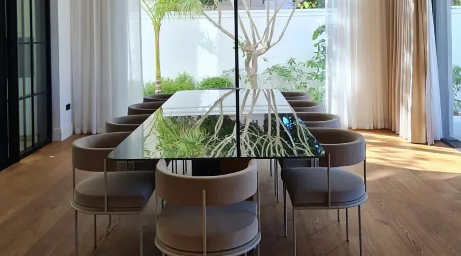 Modern dining room design furniture with a reflective glass-top table and soft upholstered chairs in a nature-inspired interior space